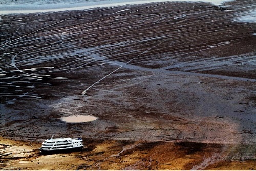 Iranduba  Amazonas 25 10 2010 RECORDE VAZANTE- SECA AMAZONAS. Barco  no meio do leito rio seco em frente a cidade de Manaus, o rio Negro sofreu a maior vazante da história. A série "Uma certa Amazônia" realizada durante a primeira década do século  21, quando os eventos extremos de cheia e vazante na Amazônia revelaram que algo de muito errado está acontecendo com o clima do planeta. Mudanças cada vez mais drásticas no regime das águas da bacia dos rios Negro e Solimões provocaram impactos como a fome, sede, doenças e mortandade de animais. O cotidiano das populações tradicionais e a paisagem amazônica mudaram definitivamente. Uma situação de extremos, onde as vazantes estão, a cada ano, se transformando em catástrofes e as cheias mostrando-se cada vez mais trágicas. Este cenário que a cada vez mais perde áreas de florestas para o agronégocio, principalmente  as plantações de soja e milho, assim como a criação de gado, além da pressão sofrida pela industria madereira em áreas de preservação permanente e também em terras indígenas, além  da exploração mineral e a ameaça pelas grandes obras de infra-estrutura do governo brasileiro fazem da Amazônia um dos ecossistemas mais frágeis perante a ação do homem.